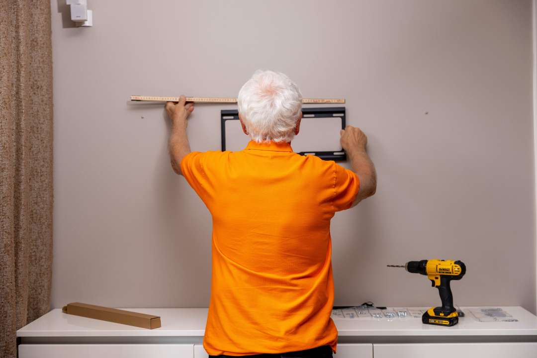 Man i orange tröja hänger upp tavla med verktyg